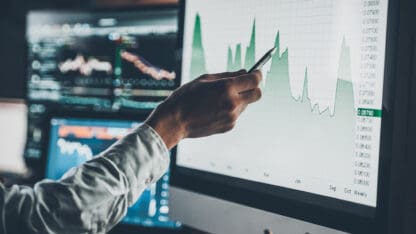 Analyst pointing with a pen at a line graph on a digital display.