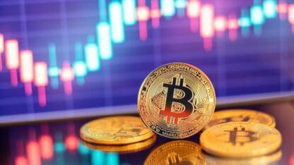 Printed physical tokens representing bitcoins in front of a digital display of box plots.