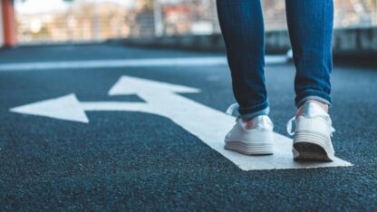 A person walking on road with on top of an arrow indicating a straight-ahead and left-turning path.