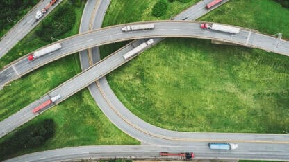 Freight trucks driving across different paths on a freeway interchange.
