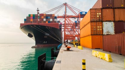 Cargo container ship moored at harbor. Loading or unloading containers with cranes.