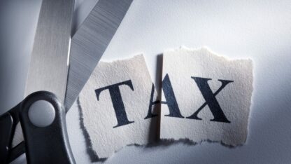 A pair of scissors that has cut through a piece of paper with the word "tax" on it.