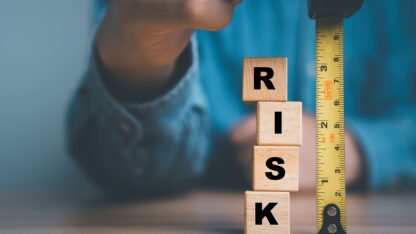 Wooden blocks spelling out the word RISK next to a tape measure.
