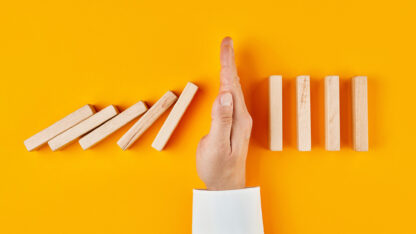 A hand blocking the path of falling dominos.