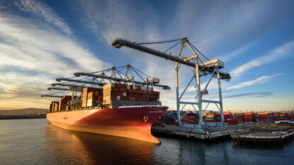 A cargo ship docked at part beneath a crane.