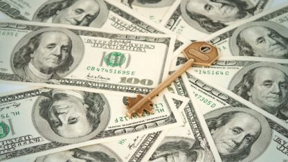 A key placed on a pile of one-hundred US dollar bills.