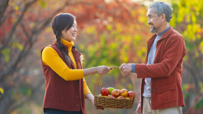 Older man and younger woman holding a basket of apples together.