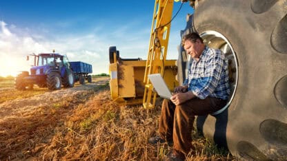 Man sitting inside the wheel of a tractor working on a laptop.