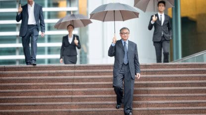 Men and women in suits walking down stairs holding umbrellas.