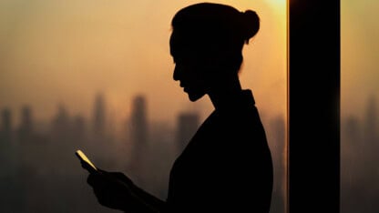Silhouette of young woman using smartphone next to window with cityscape