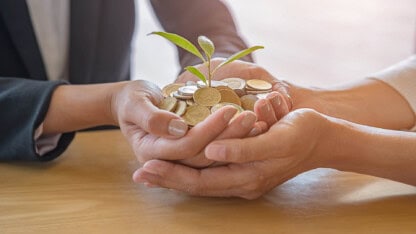 Hands cupping a collection of coins with a small green plant sprouting from the center, symbolizing savings and sustainable investment