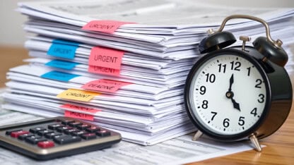 An alarm clock standing next to a stack of papers and a calculator