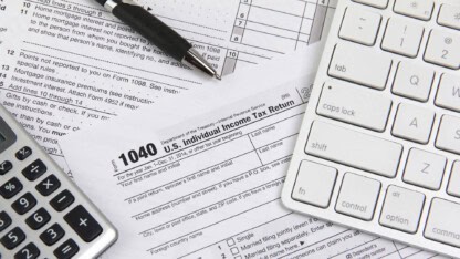 Tax forms beneath a pen, calculator, and keyboard.